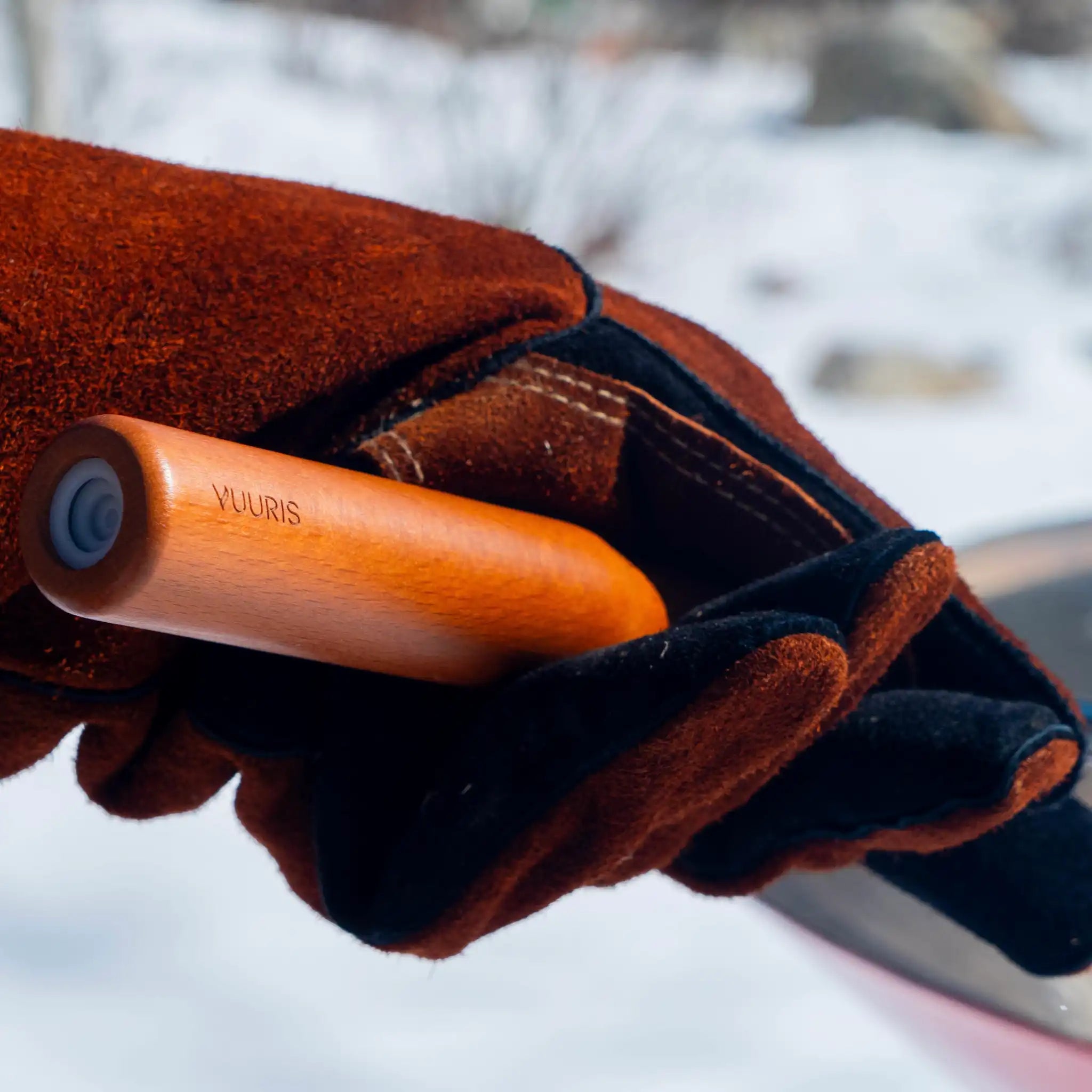 A close up of the Vuuris gloves holding the handle of the blow poke. the handle is in wood with a Vuuris logo engraved.
