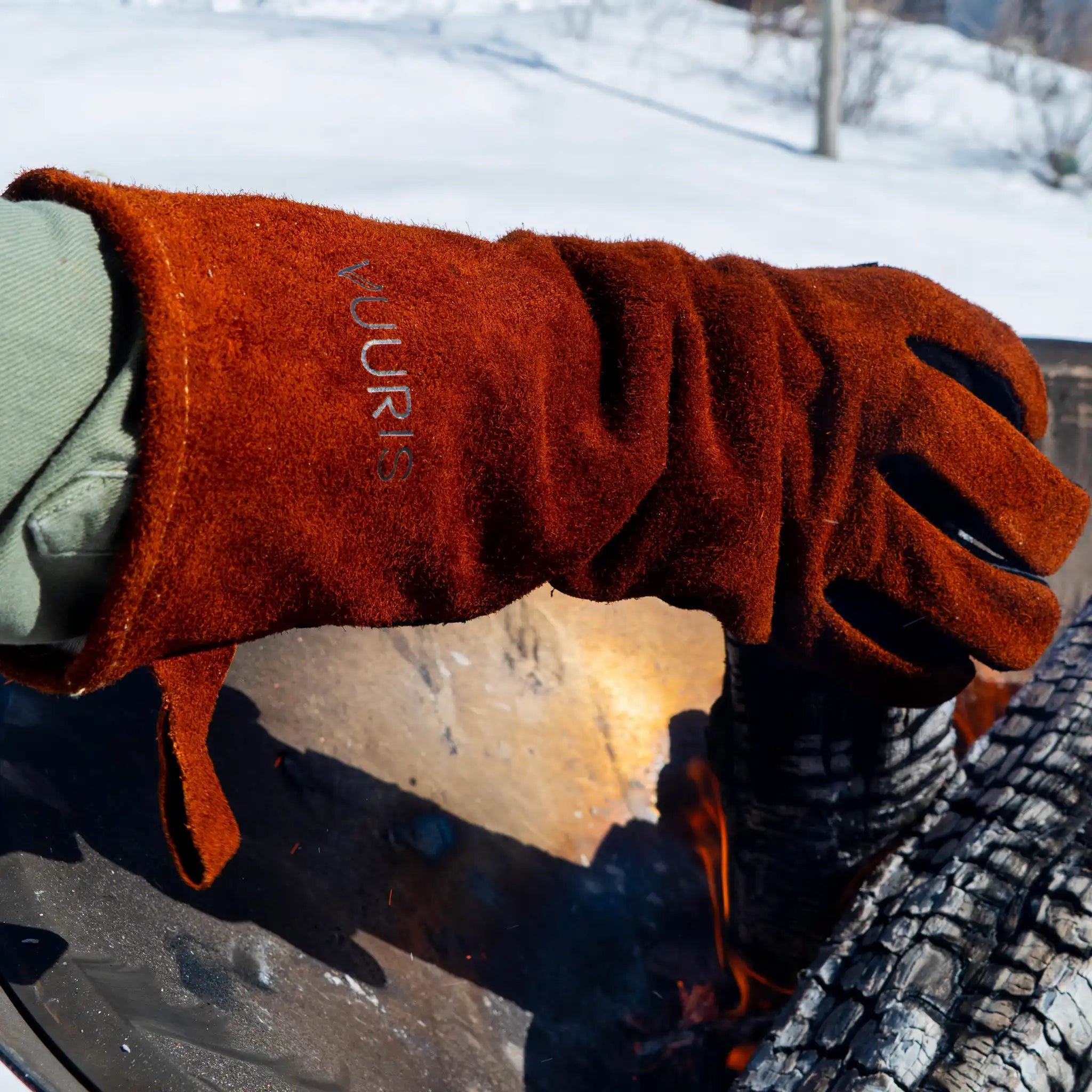 Vuuris heat-resistant leather gloves in use, demonstrating fire-side protection and dexterity near the Vuuris fire pit, while holding a burning log of wood