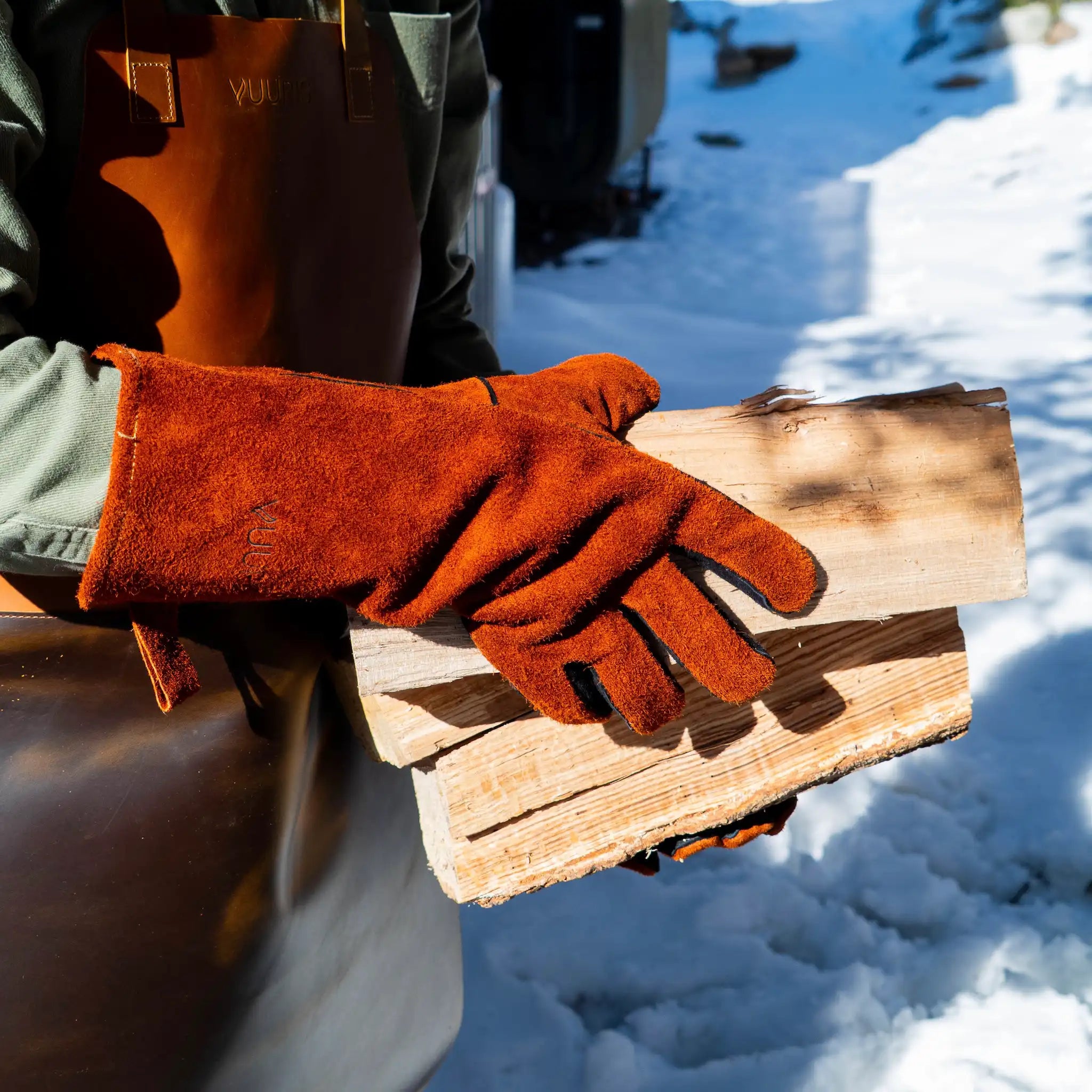 Vuuris heat-resistant leather gloves in use, demonstrating fire-side protection and dexterity near the Vuuris fire pit, while holding a burning log of wood