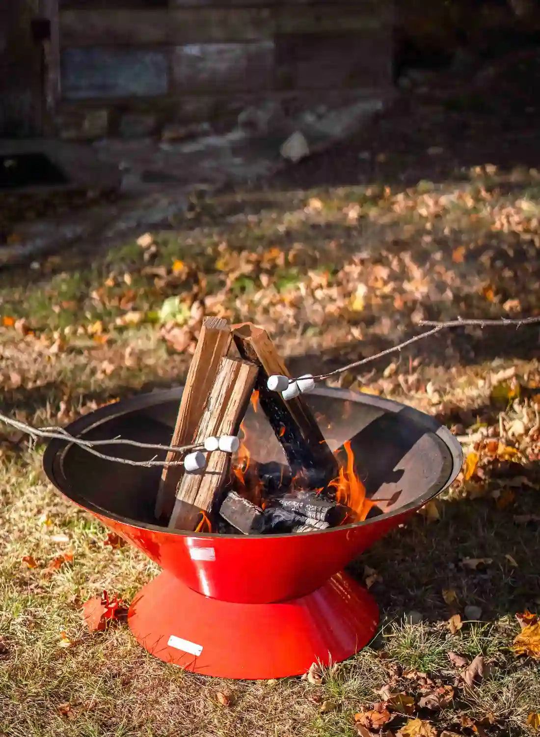 roasting marshmallows over the orange Vuuris Tiger outdoor fire pit, showcasing the authentic wood-fired open-fire experience on a grassy soil with some leaves on it