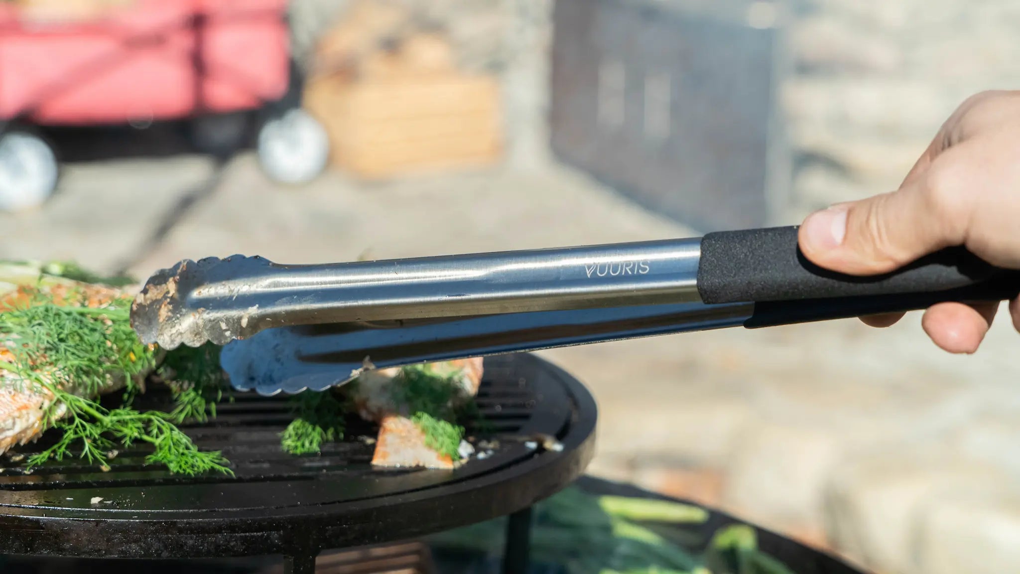 Vuuris long-handle stainless steel tongs in use at the Vuuris outdoor fire pit, demonstrating the 16-inch extended reach for safe open-fire cooking