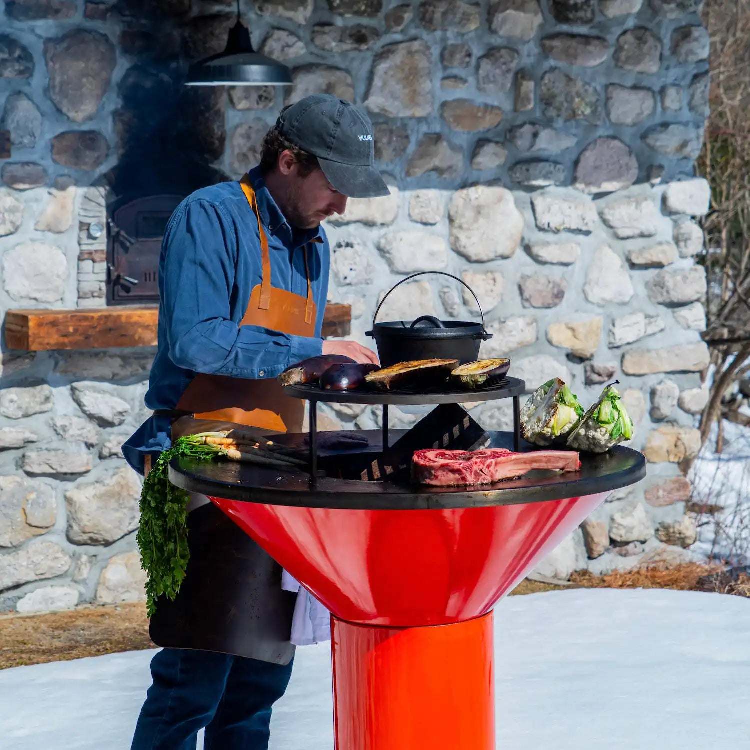 Vuuris founder cooking on Vuuris Tiger large base fire centerpiece with background of snow and stone house