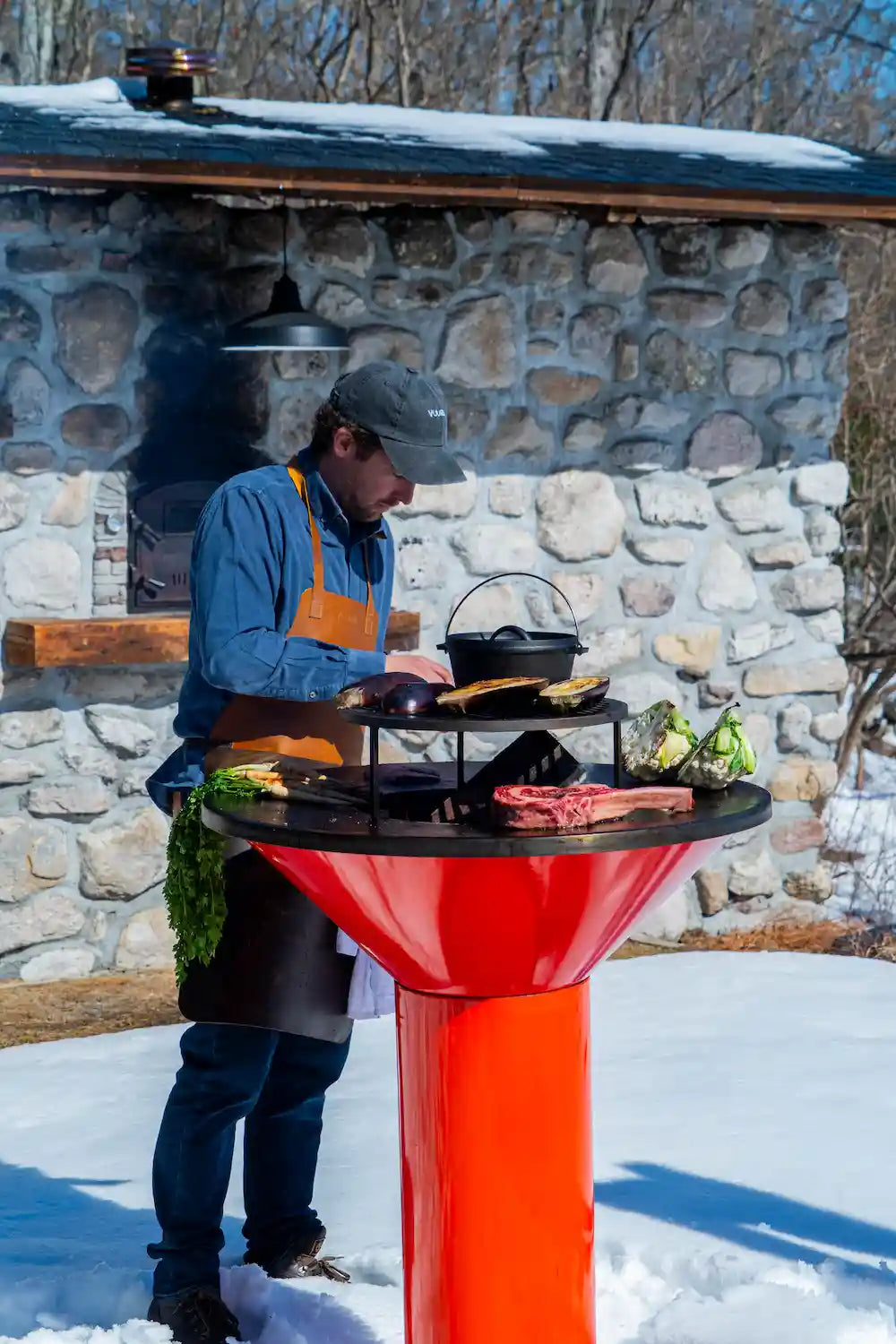 Vuuris founder cooking on Vuuris Tiger large base fire centerpiece with background of snow and stone house
