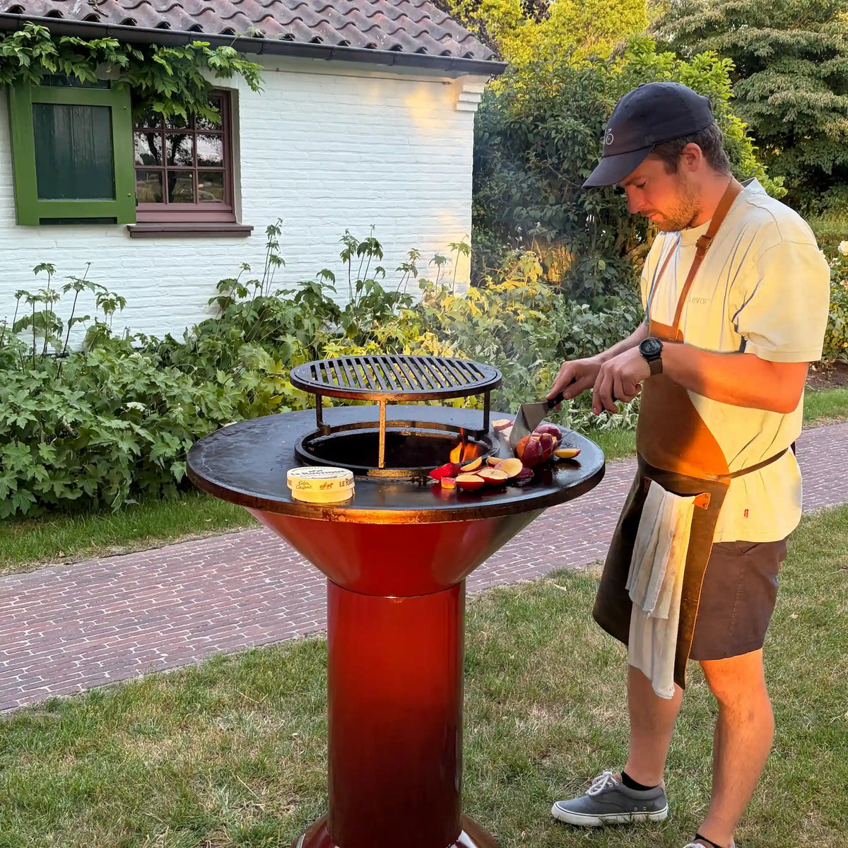 Garnet Vuuris bbq with the food bumper and grill with a man flipping peaches on the cooking plate with a white house in the background