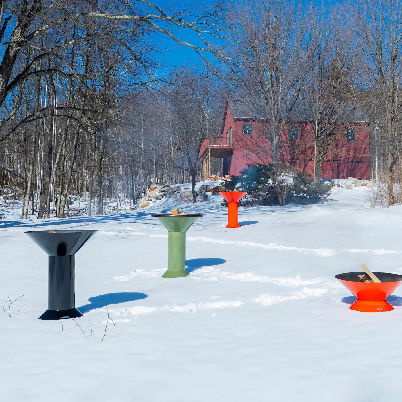 A wide shot of a field full of snow with a red house in the background with 4 Vuuris products that are on fire, a orange Tiger, green Sage and black Onyx in the large base setup and one orange Tiger in small base setup
